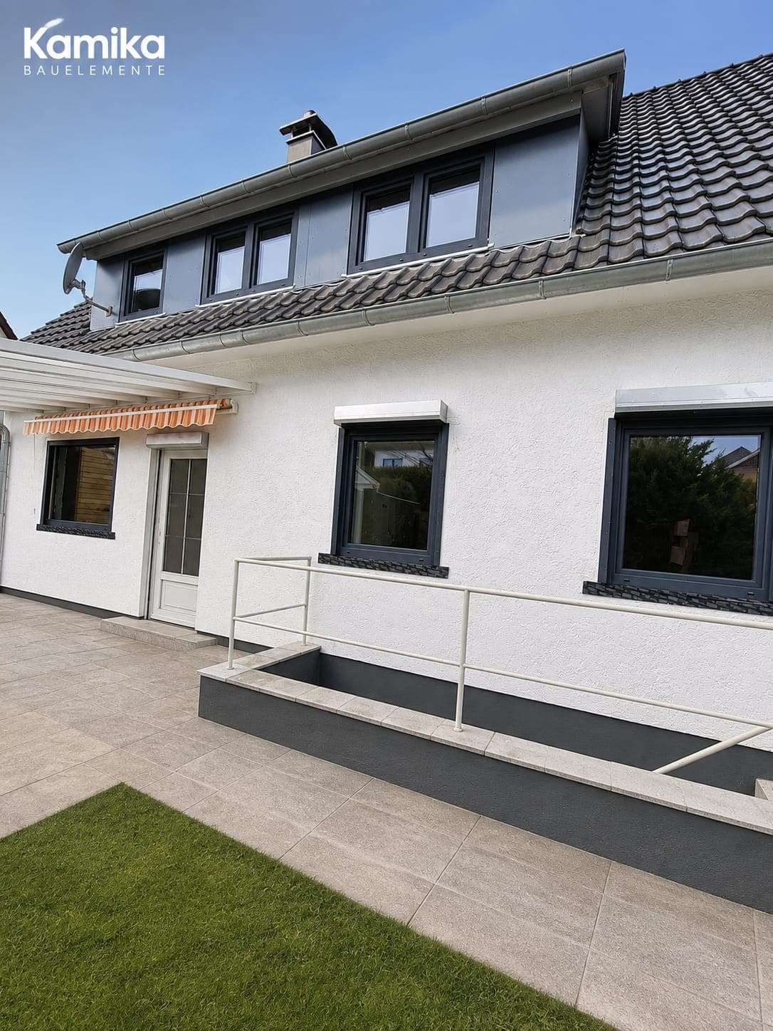 Gartenfassade mit Anthrazit-Fenstern, weißer Terrassentür und Markise über der Terrasse