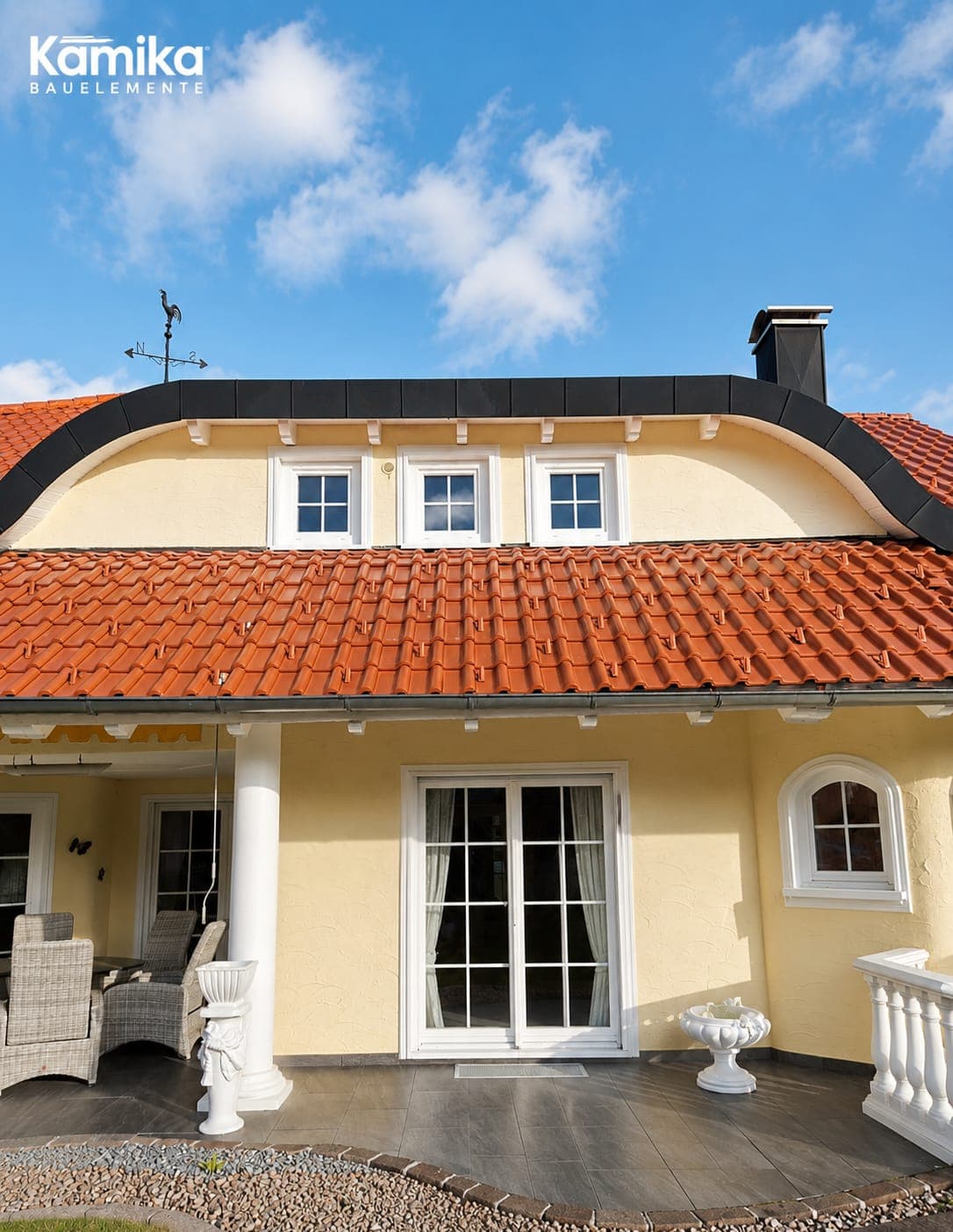 Gelbes Haus mit geschwungenem Dach, weiße Sprossenfenster und zweiflügelige Terrassentür